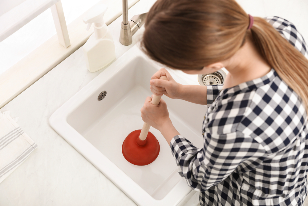 oman using plunger to unclog sink drain in kitchen, above view